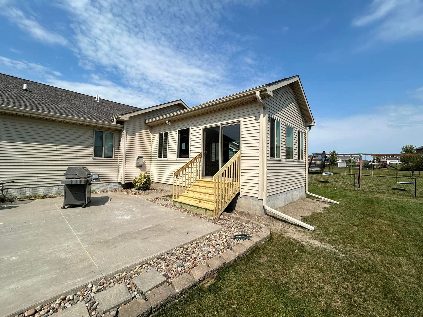 A completed addition with new siding and trim opening onto a freshly poured concrete patio.