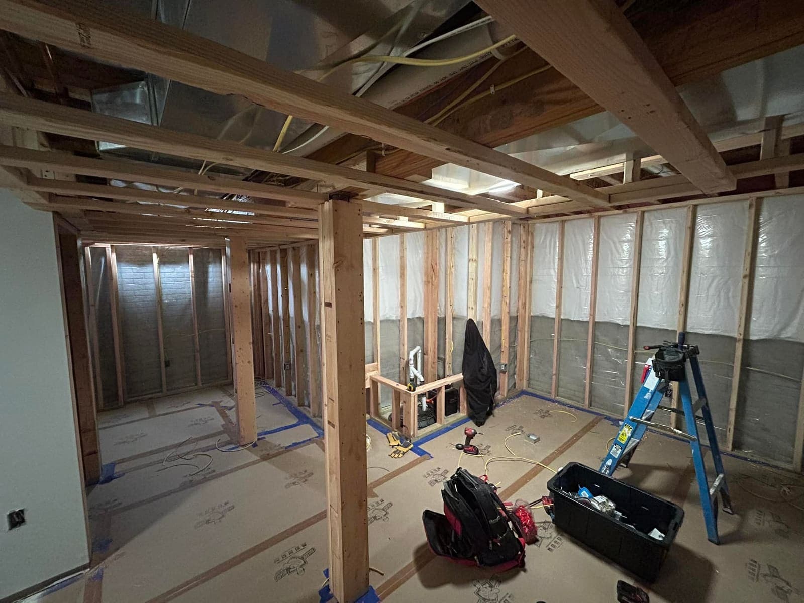 A basement part framed, with insulation and a vapor barrier against the foundation wall and the joists still open overhead.