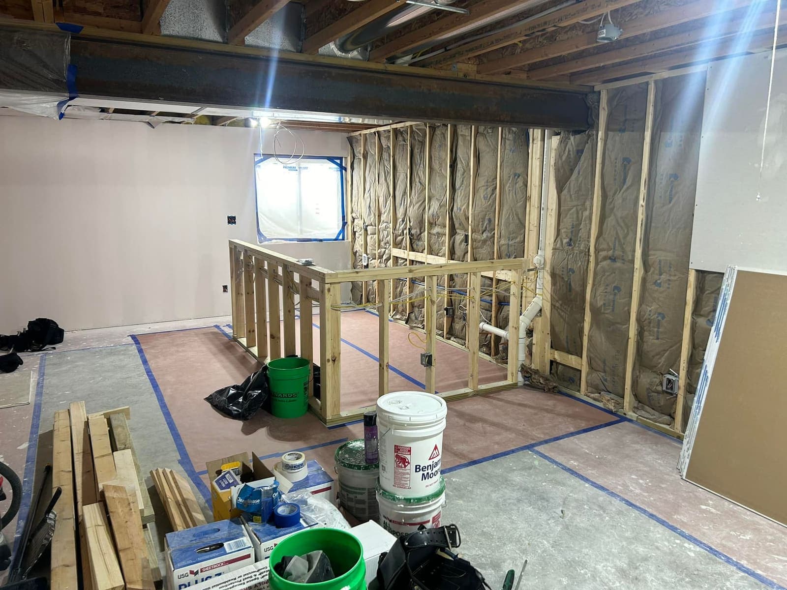 Basement partition walls framed around an egress window opening, with the floor papered and taped off.