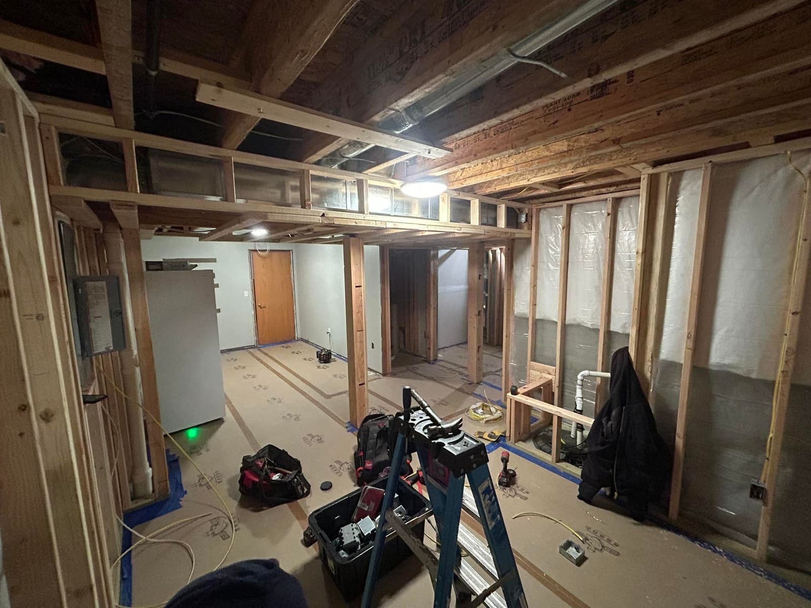 A framed basement with the ductwork, wiring and beams still exposed overhead before anything is boxed in.