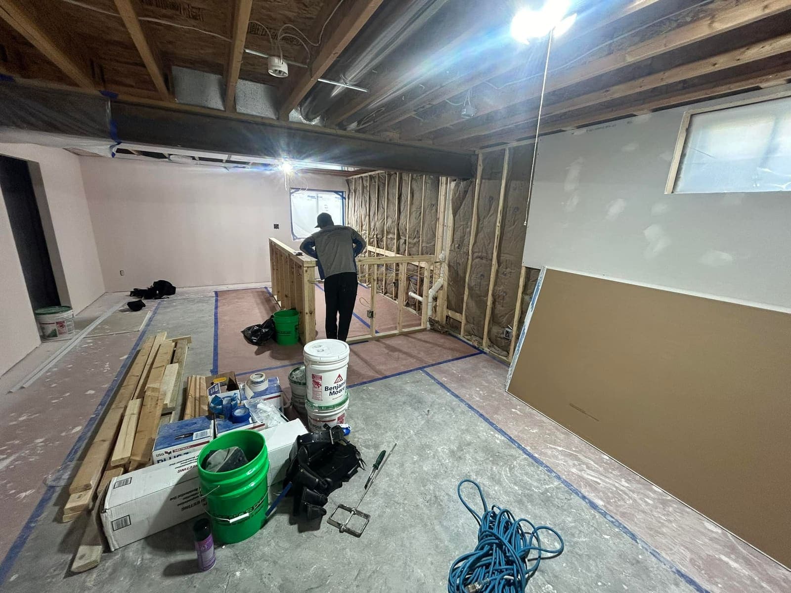 Drywall being hung in a basement, with sheets stacked and the framing still open on the far wall.