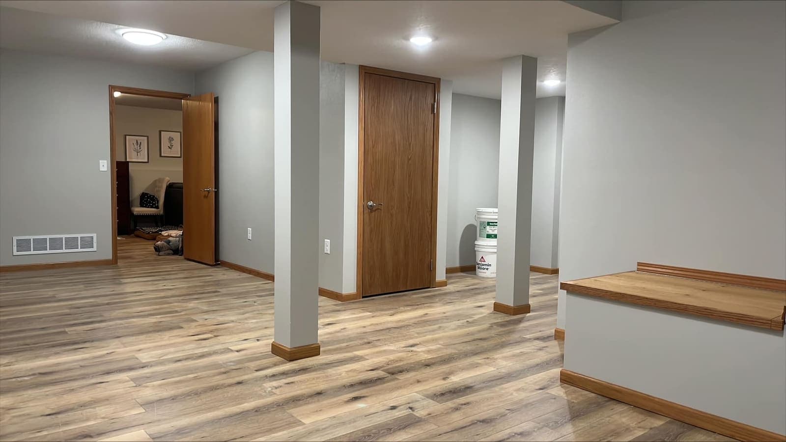 A finished basement with structural posts wrapped in stained wood and plank flooring running past them.