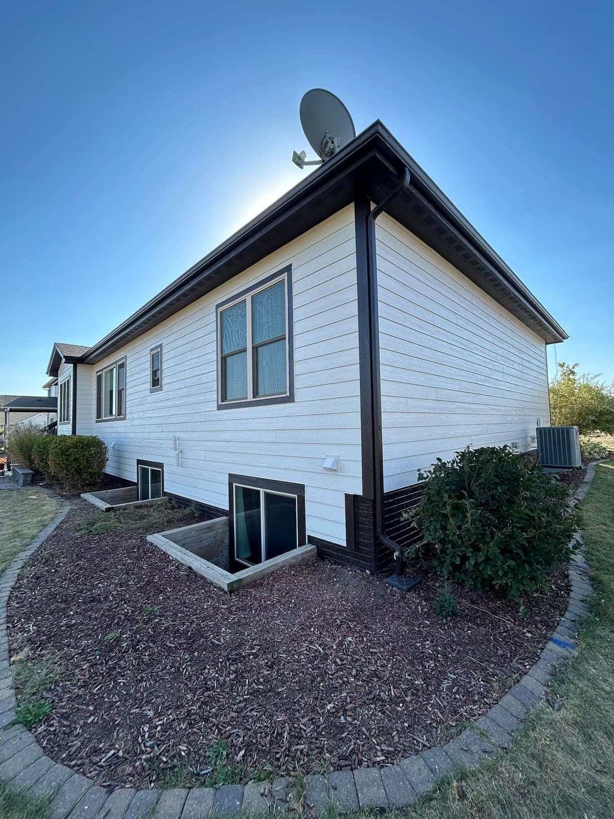 Two egress window wells set into the grade against the side of a house.