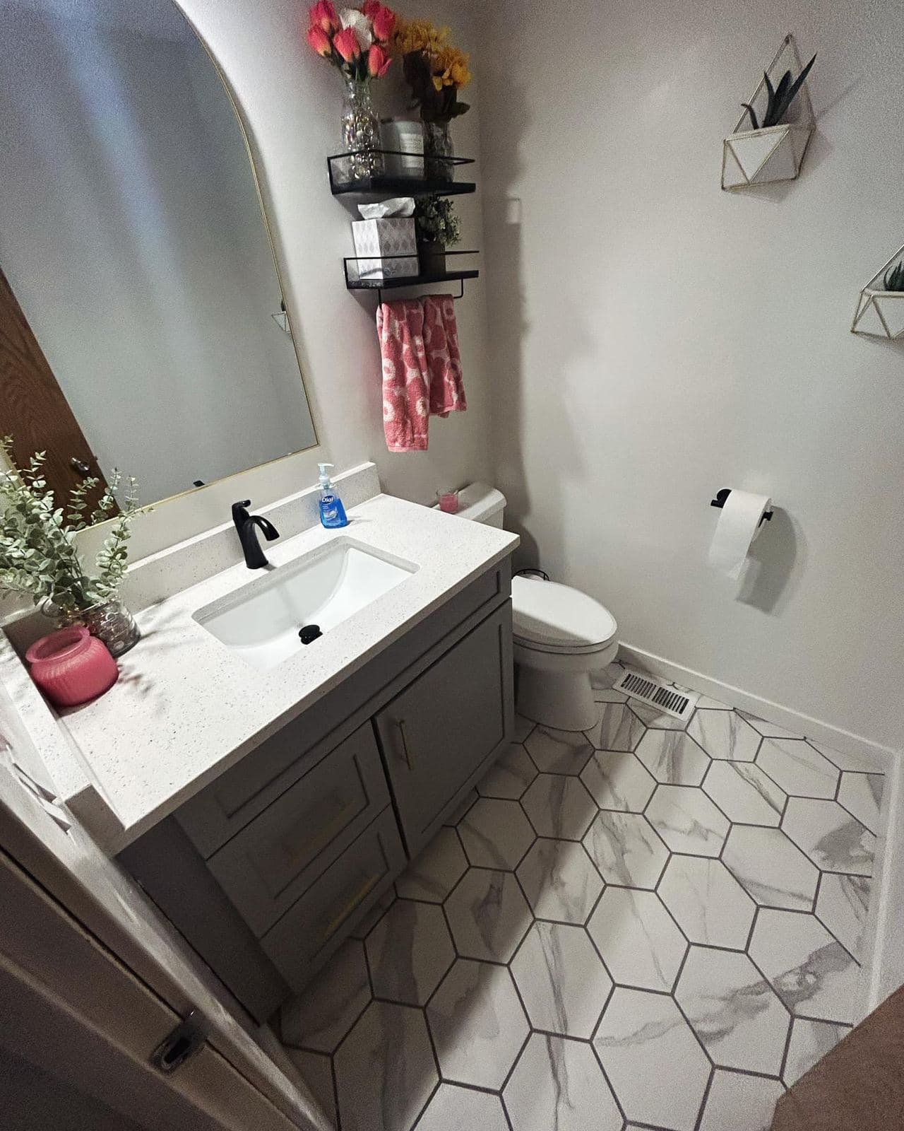 A bright bathroom with a white quartz vanity top, matte black faucet and a white hexagon tile floor.
