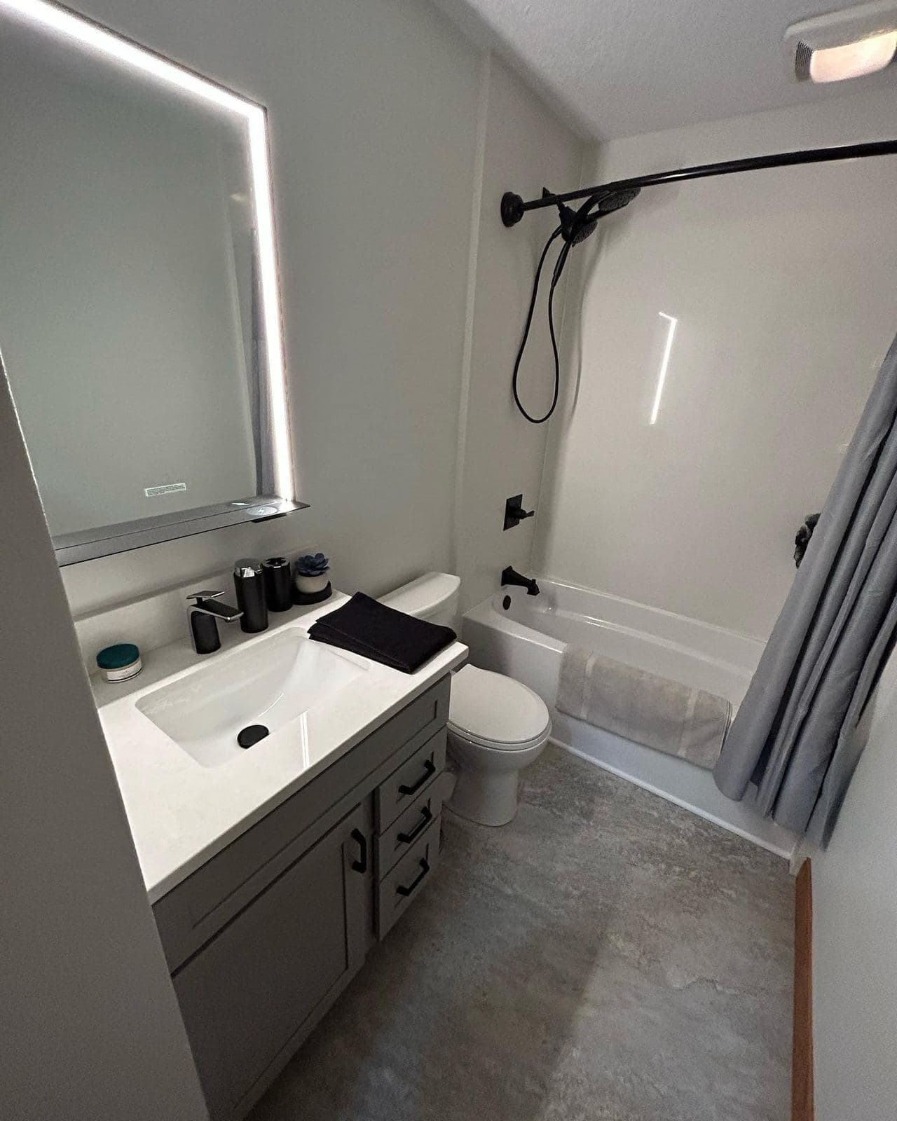 A finished bathroom with a backlit mirror, matte black fixtures and a tub and shower combination.
