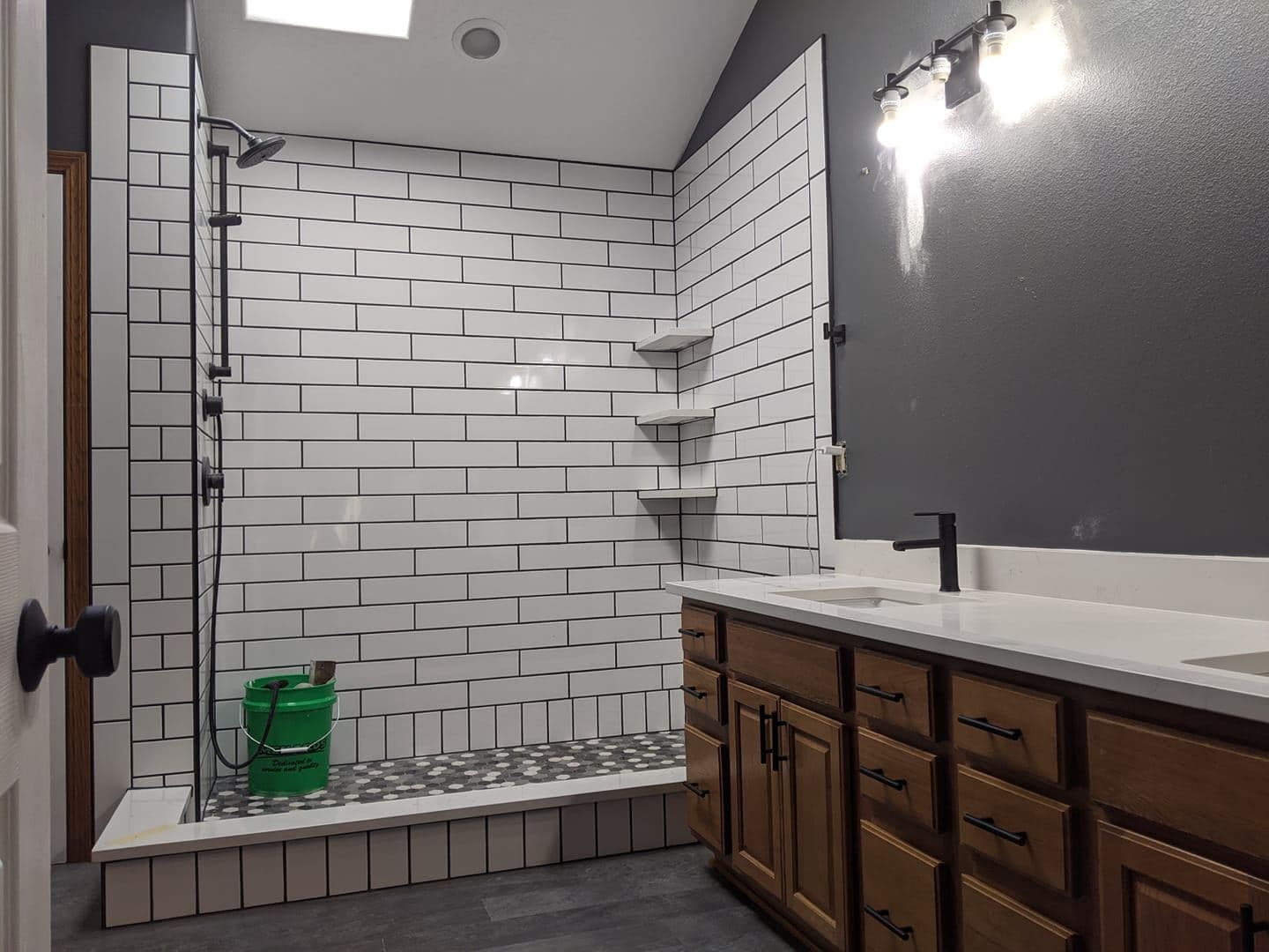 A walk-in shower lined in white subway tile with a built-in niche, beside a dark wood vanity with a white top.