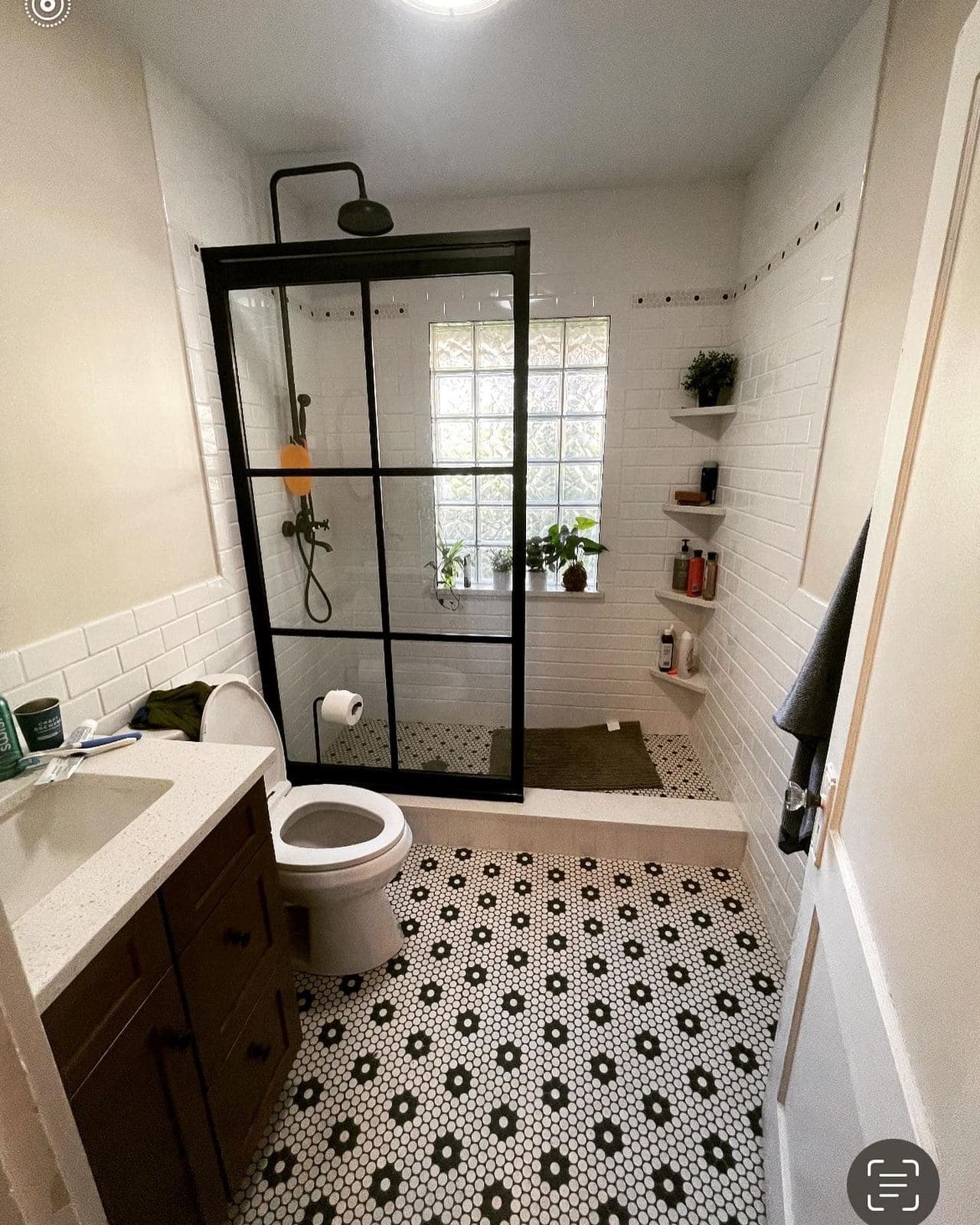 A walk-in shower behind a black-framed glass panel, with white subway walls and a black-and-white hexagon tile floor.