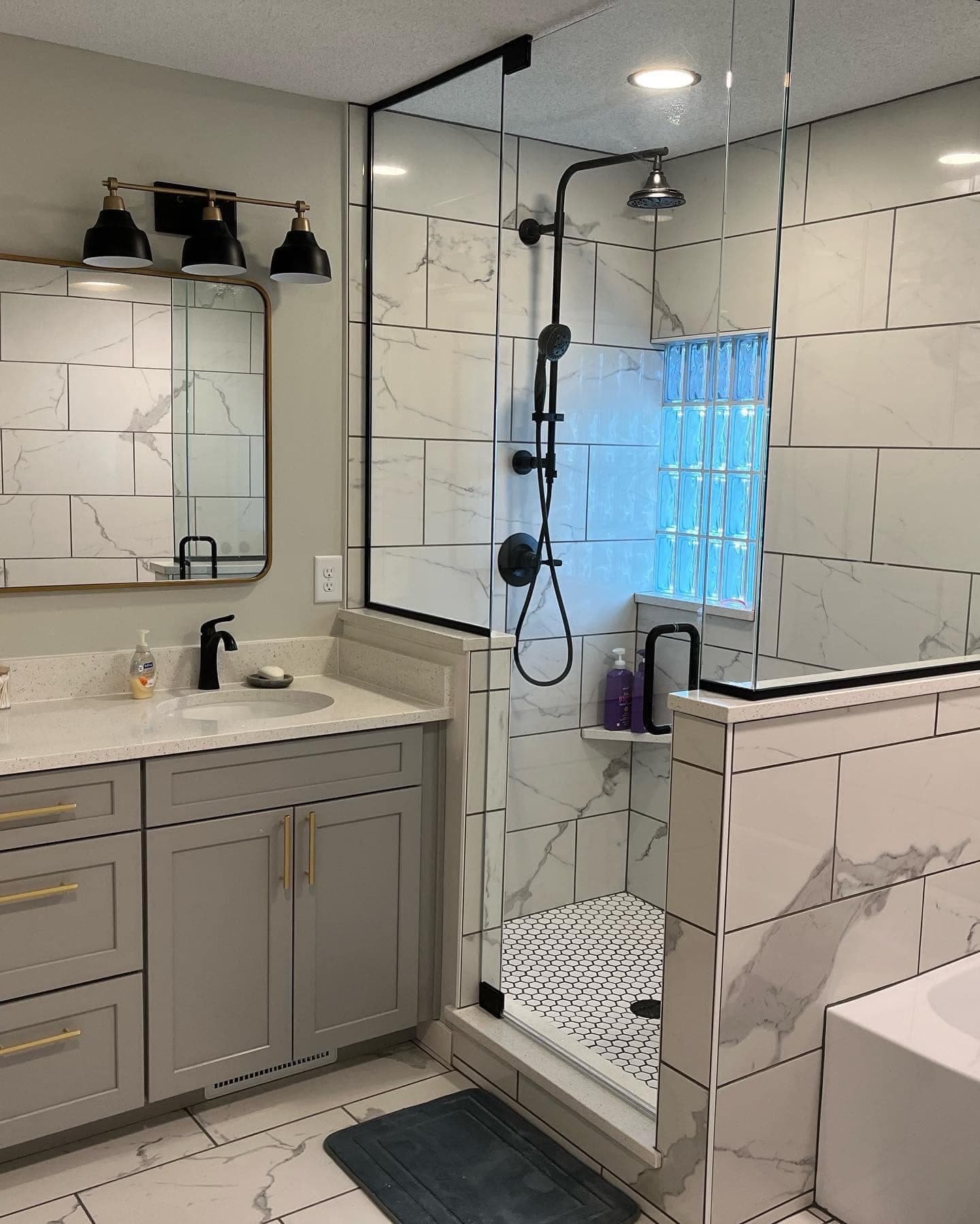 A marble-look tiled shower with matte black fittings and a glass block window
