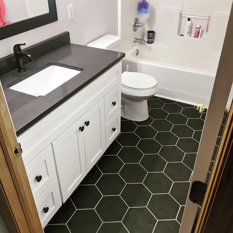 A bathroom with black hexagonal floor tile and a white vanity