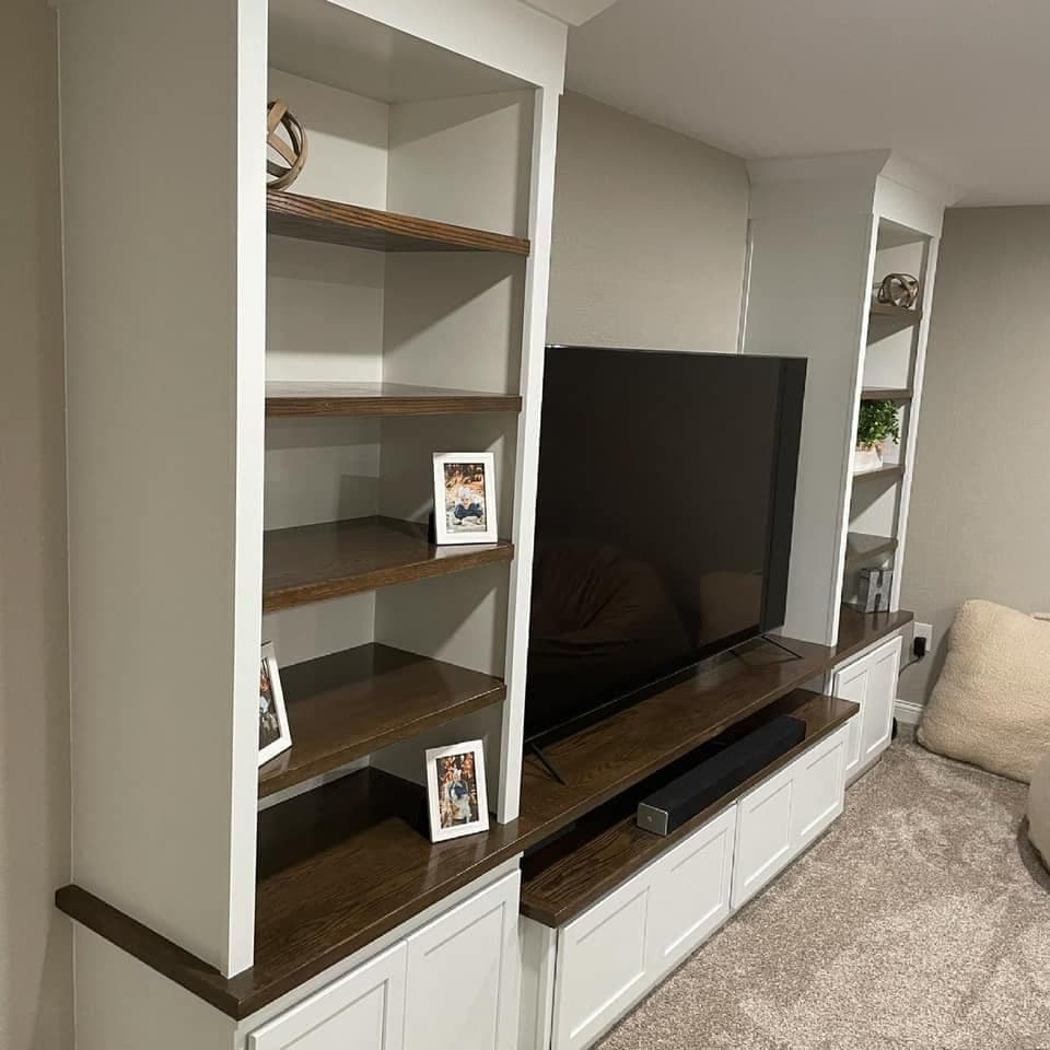 A built-in media wall in white painted cabinetry with dark stained oak shelves and counter.