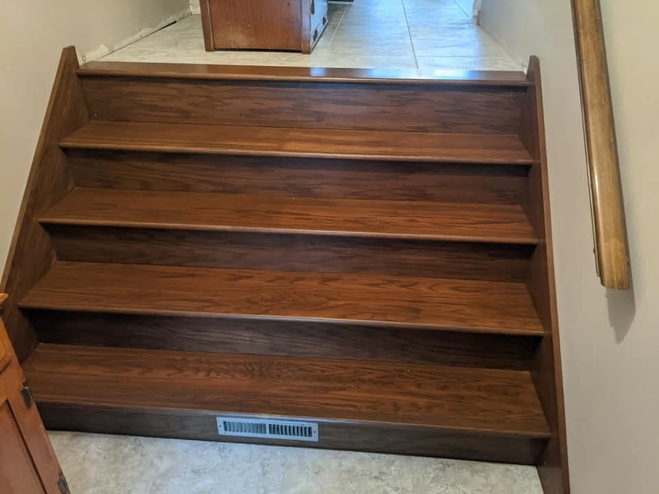 Stained oak stair treads and risers seen from above, landing on a tiled floor.