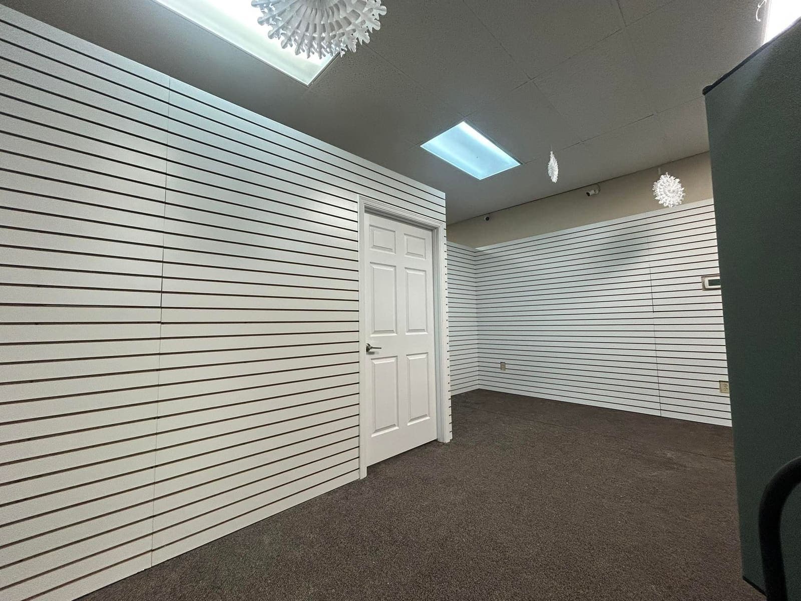 A finished retail fit-out with slatwall to two sides, a suspended ceiling and new carpet.