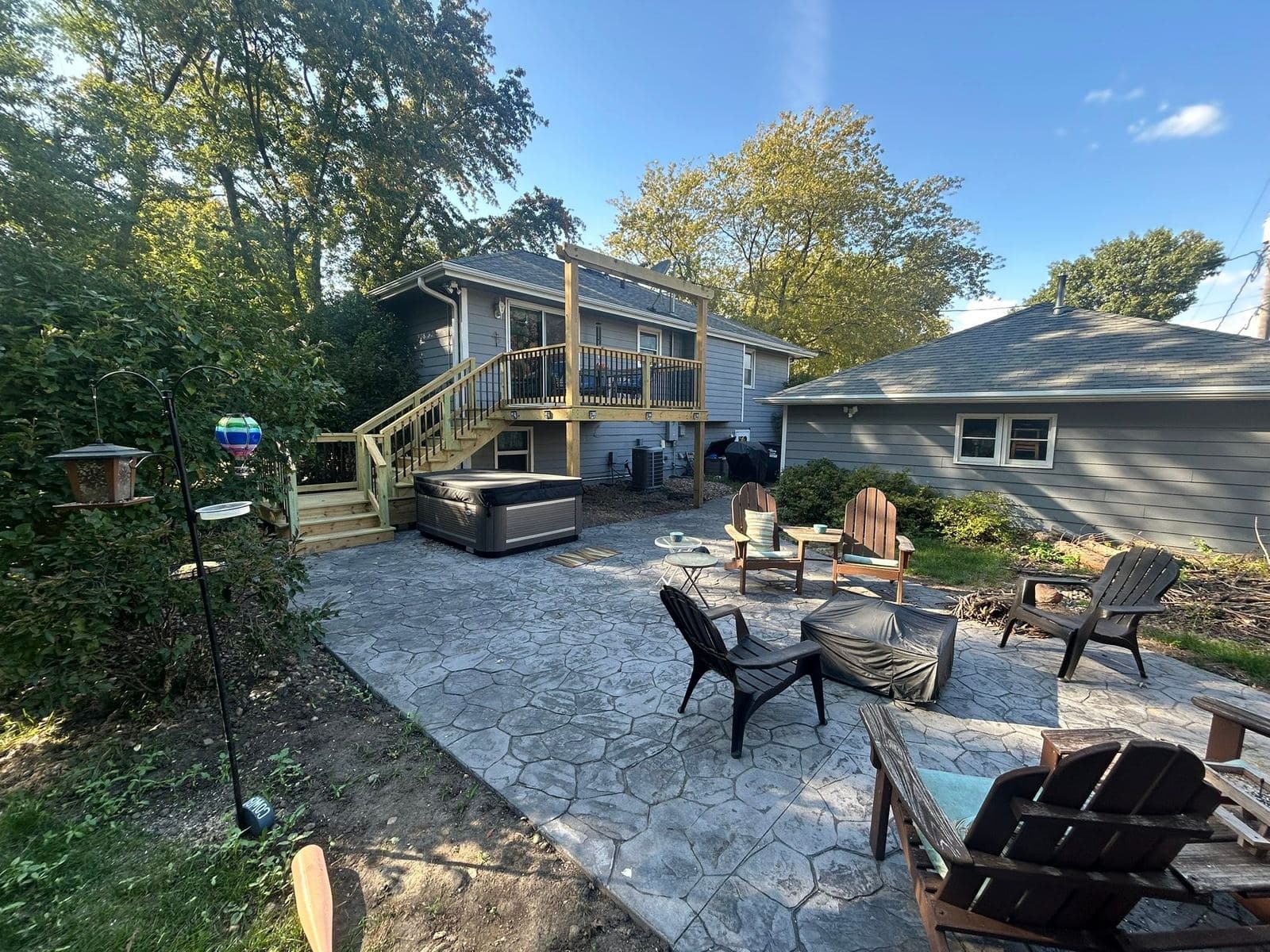 A stamped concrete patio furnished with Adirondack chairs around a fire pit, edged by lawn and landscaping.