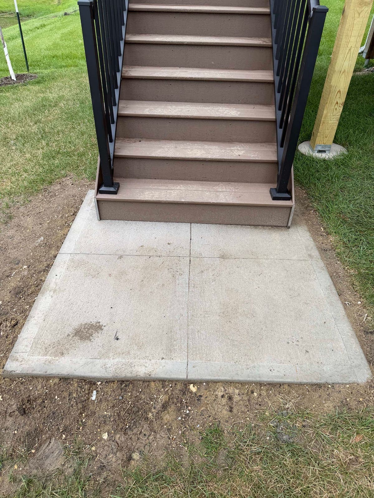 A new concrete landing pad placed at the foot of a deck staircase.