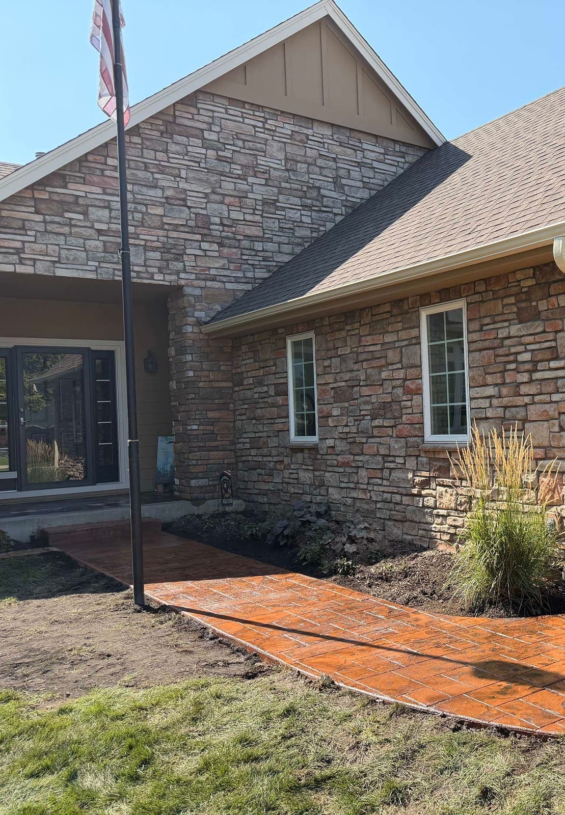 A coloured, stamped concrete walk curving to the front door of a stone-fronted house.