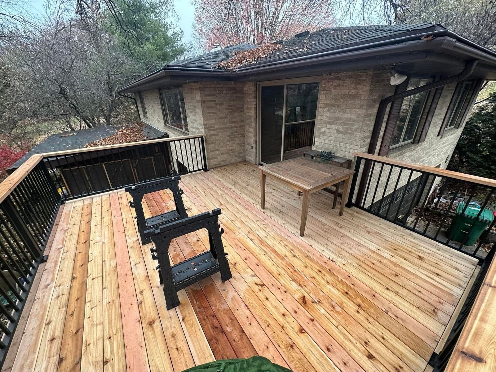 A wide cedar deck with black metal balusters wrapping the back of a home, with a picnic table and open stair access to the yard.