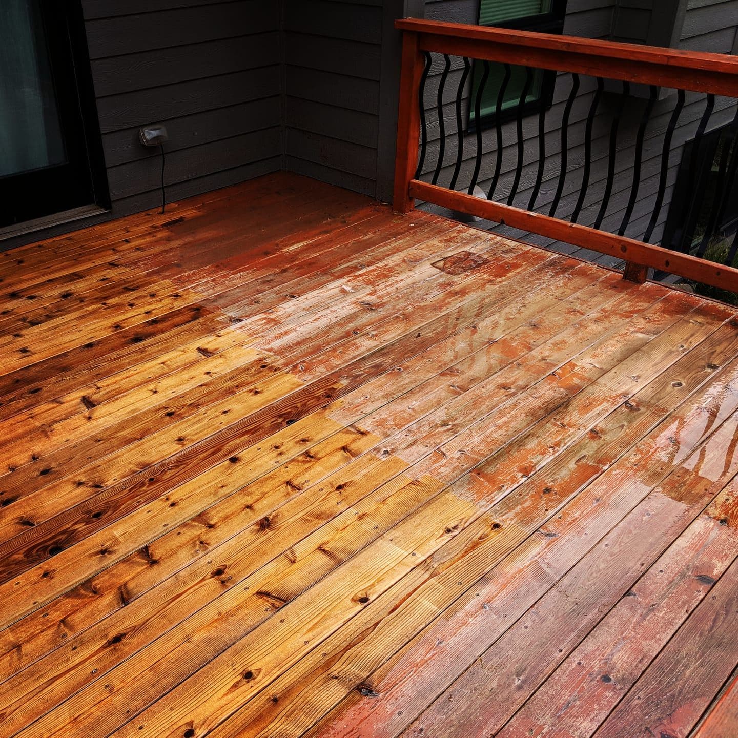 Close view of newly stained cedar decking boards running to a dark wood railing, showing the grain and even stain coverage.