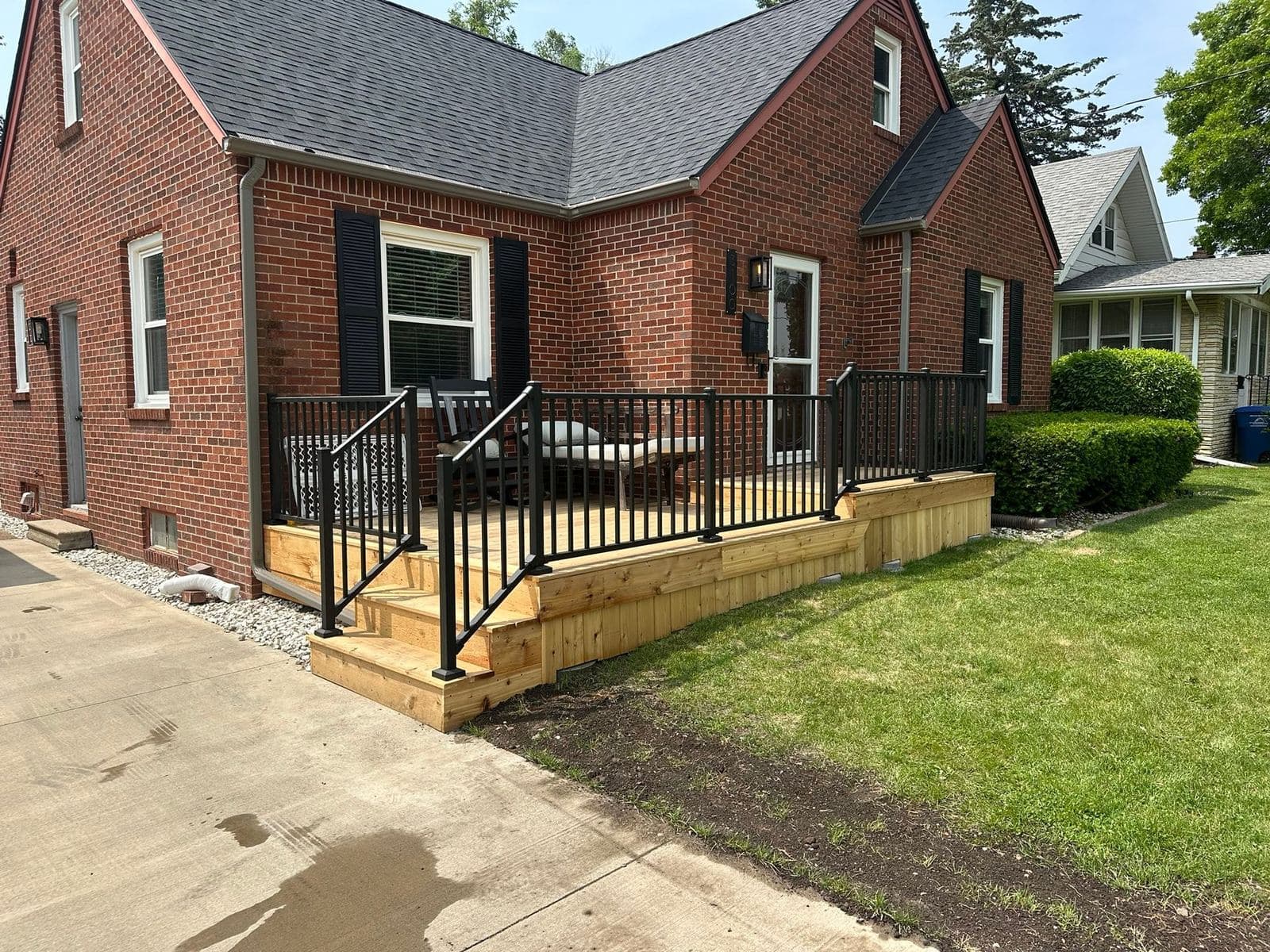 A new front porch deck with black metal railing and framed skirting on a red brick home, finished level with the walkway.