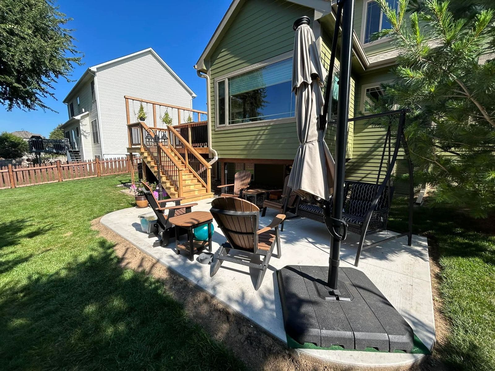 A raised deck connecting down to a paver patio with outdoor seating and a market umbrella, set between two houses.
