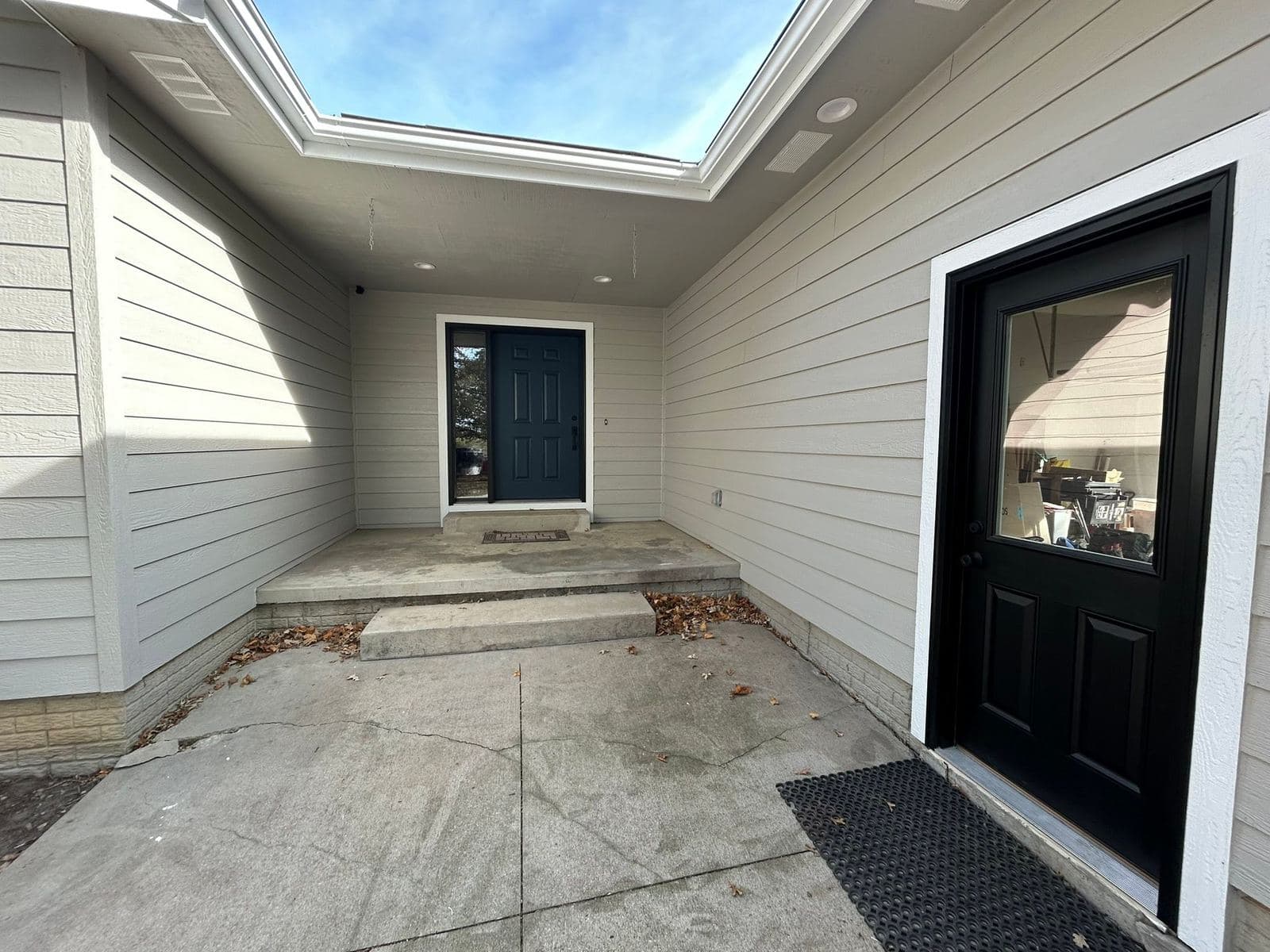 A black entry door with a full-height sidelight, set under a covered porch with recessed lighting.