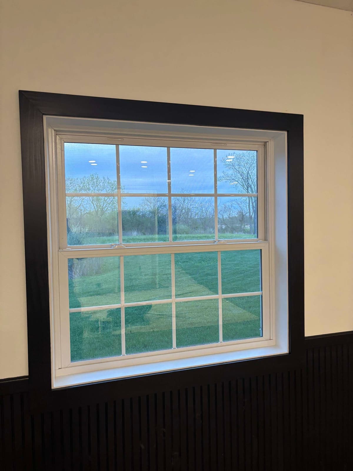 A new double-hung window finished with black trim above black wainscot.