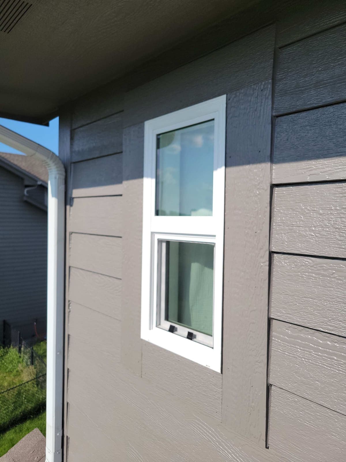 A new window fitted and trimmed in fresh grey siding, seen from outside.