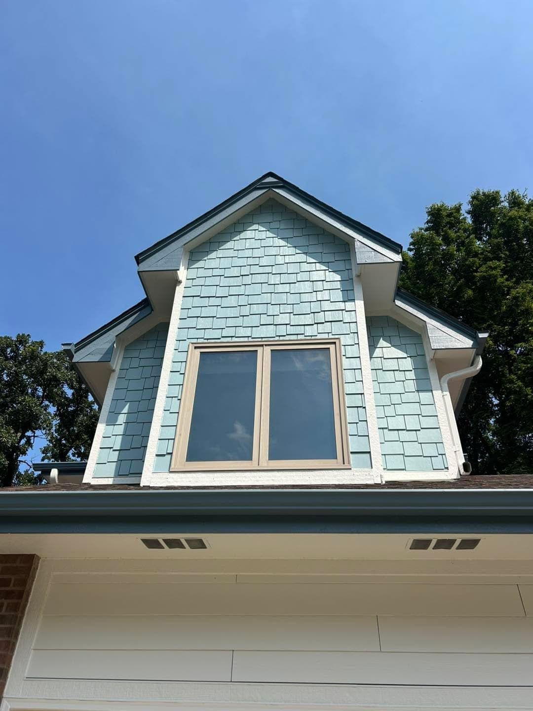 A dormer with a new window and blue shake siding around it.