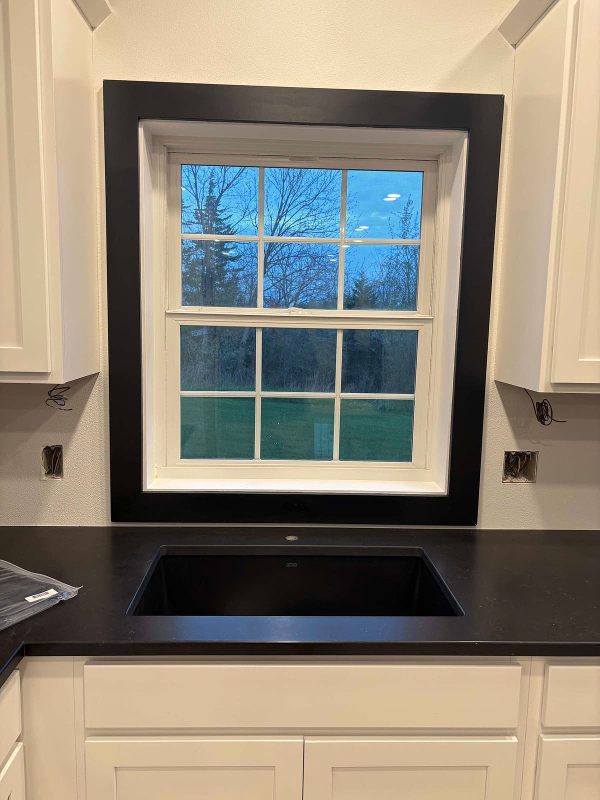 A new kitchen window with black trim above a black sink and white cabinets.
