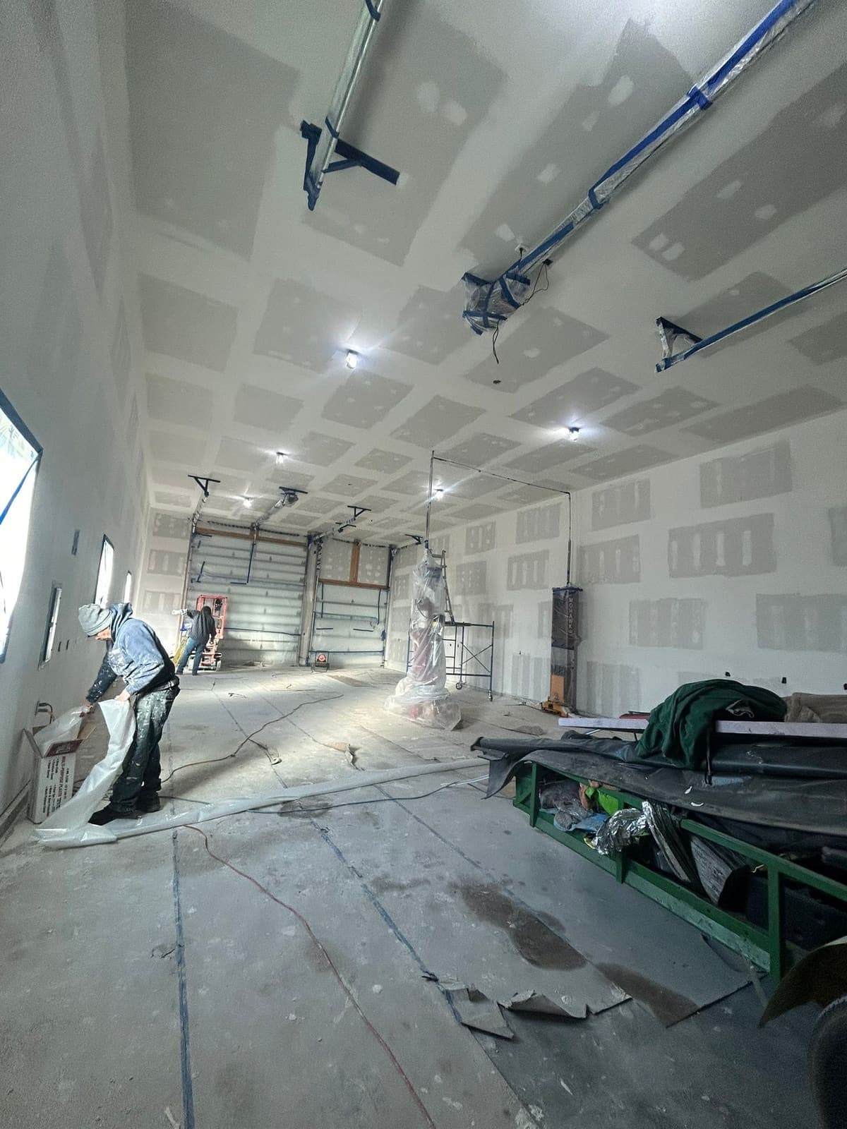 Drywall being hung and screwed off across the walls and ceiling of a large garage.