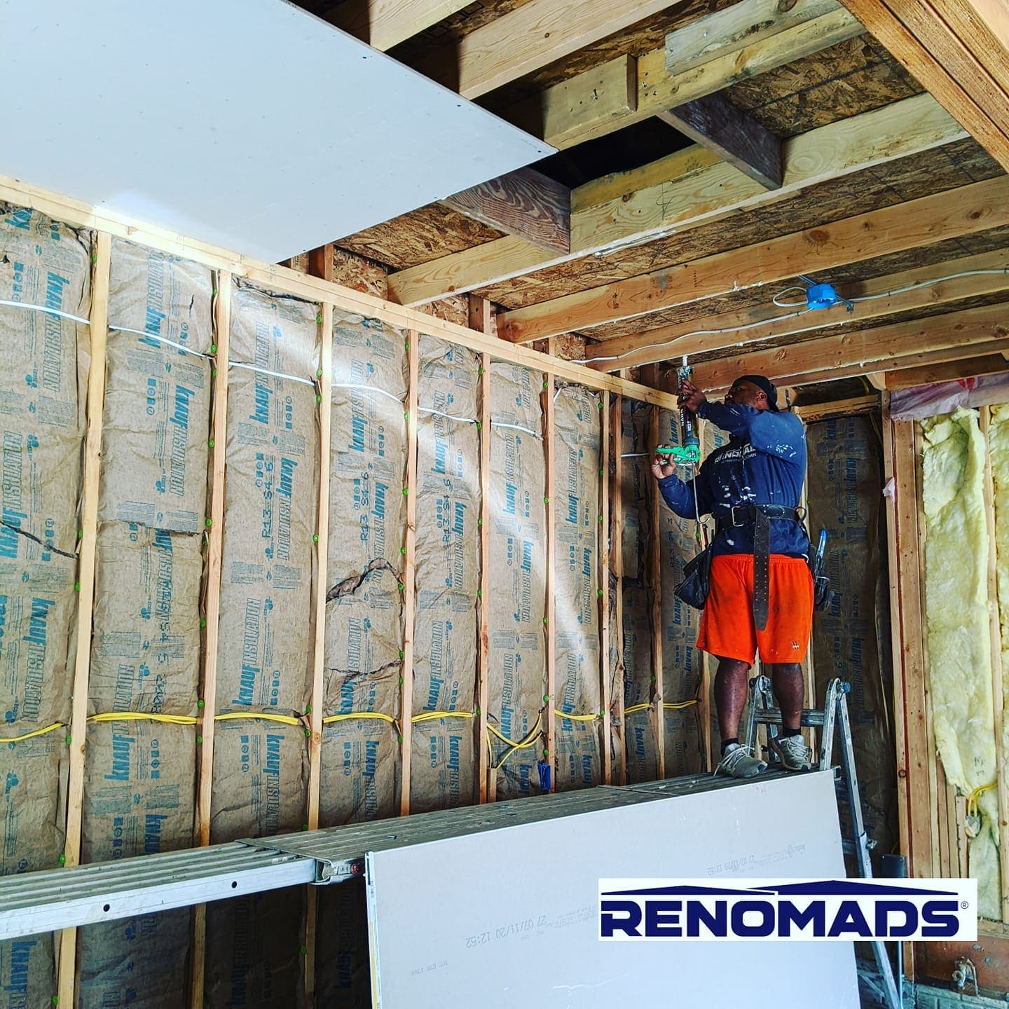 A crew member on a lift fastening a ceiling sheet, with the wall insulated behind him.
