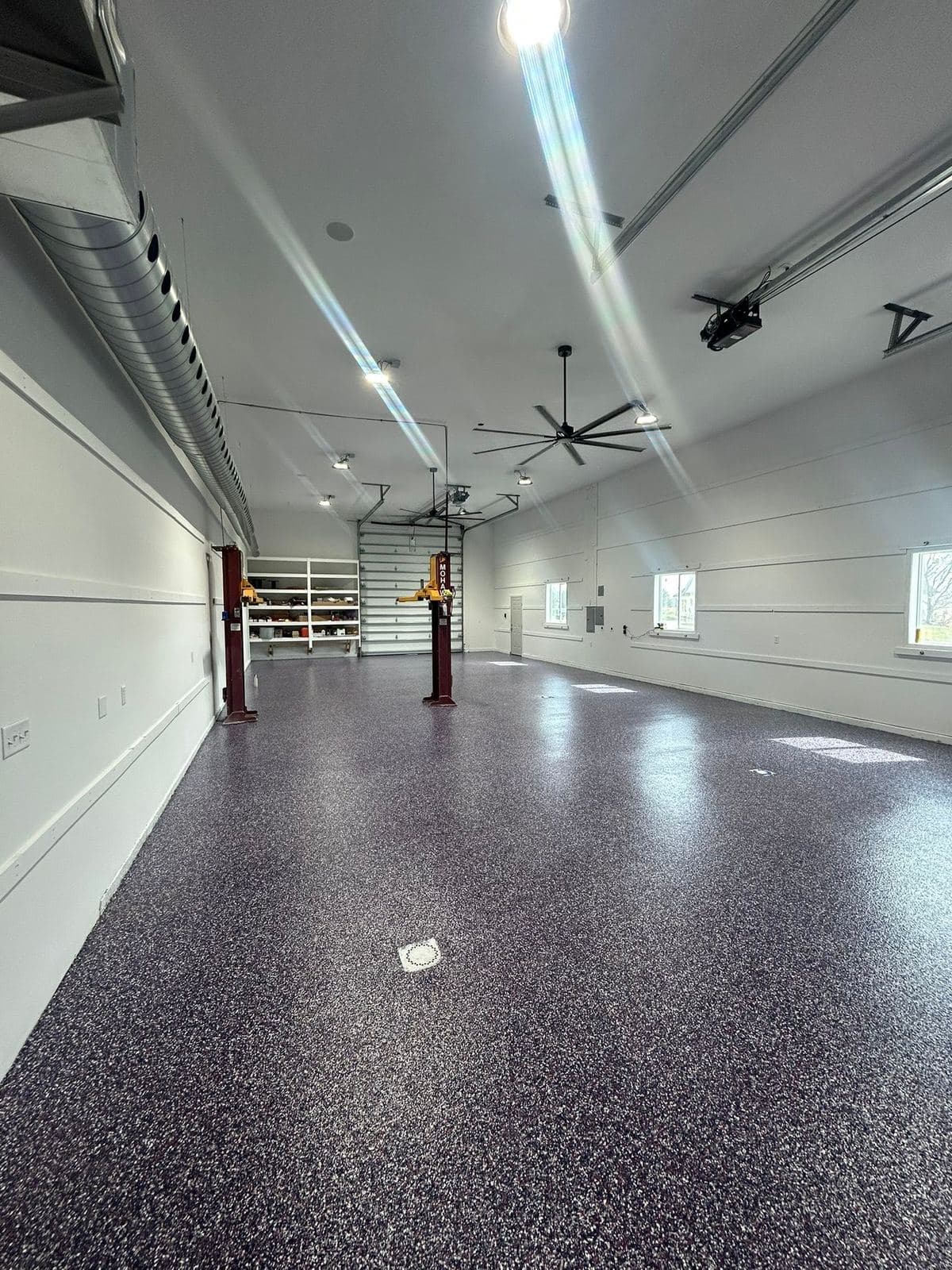 A finished garage with a speckled epoxy floor, LED strip lighting overhead and a large ceiling fan.