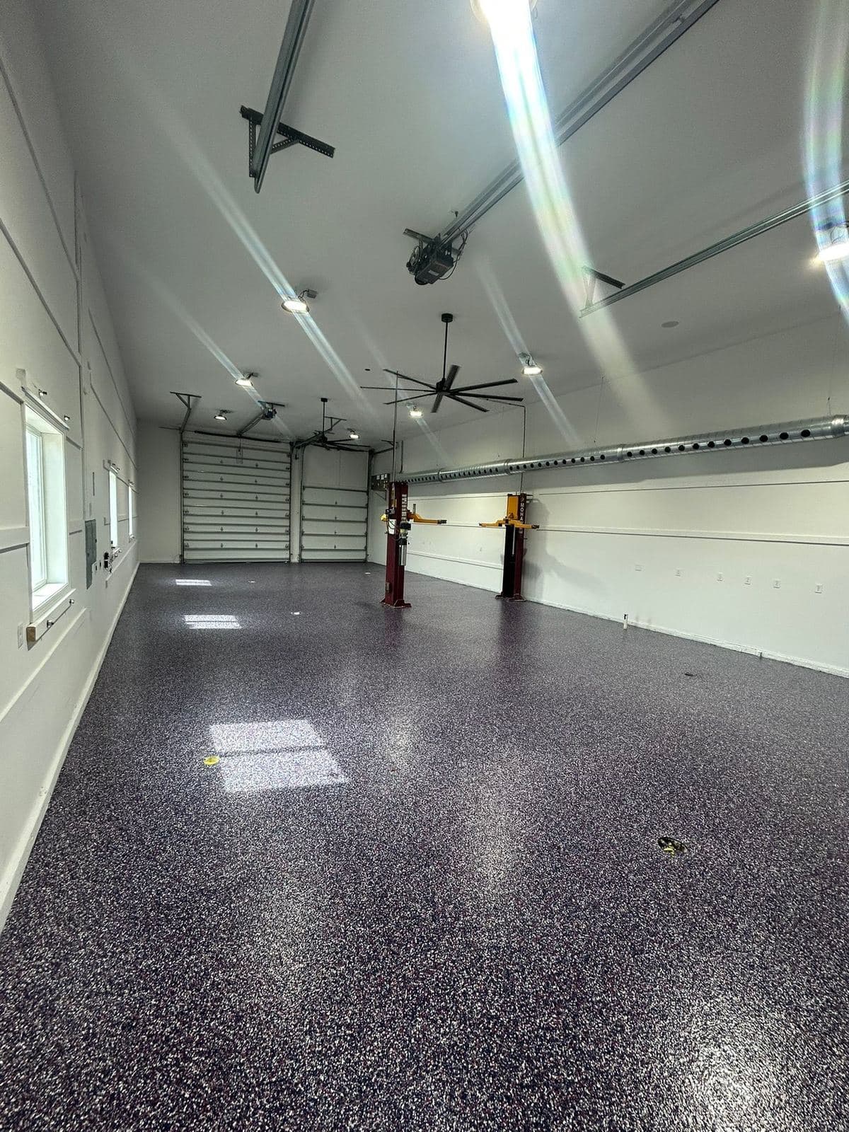 Wide view of a finished garage lit by continuous LED strips, with epoxy flooring and an overhead door.