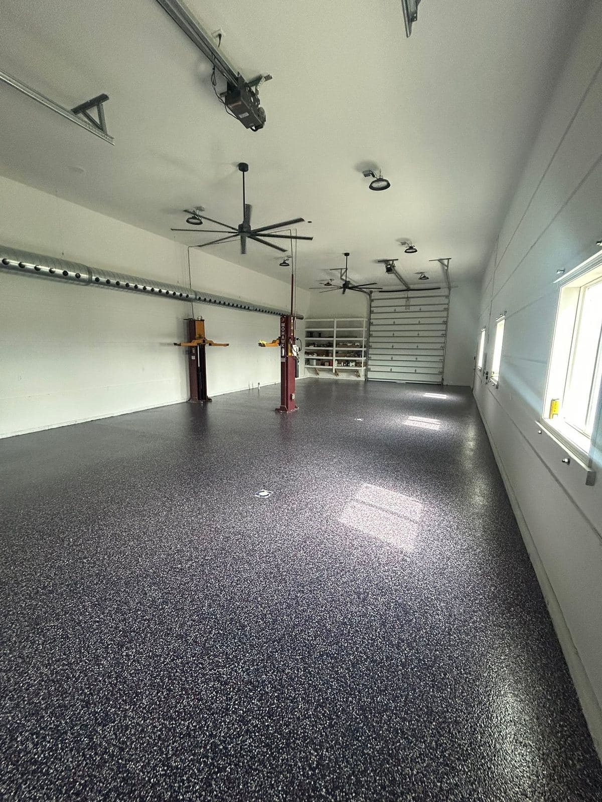 LED strip lighting and a ceiling fan installed across a finished garage ceiling above an epoxy floor.