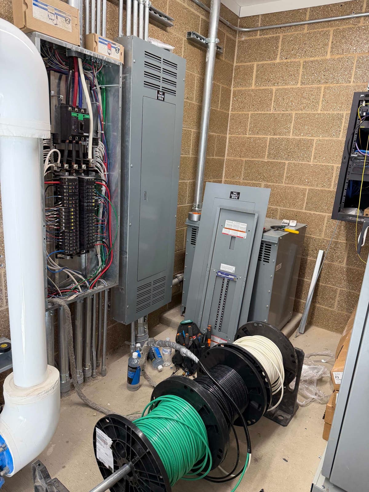 A commercial electrical room with panels, a disconnect and conduit runs on a block wall.