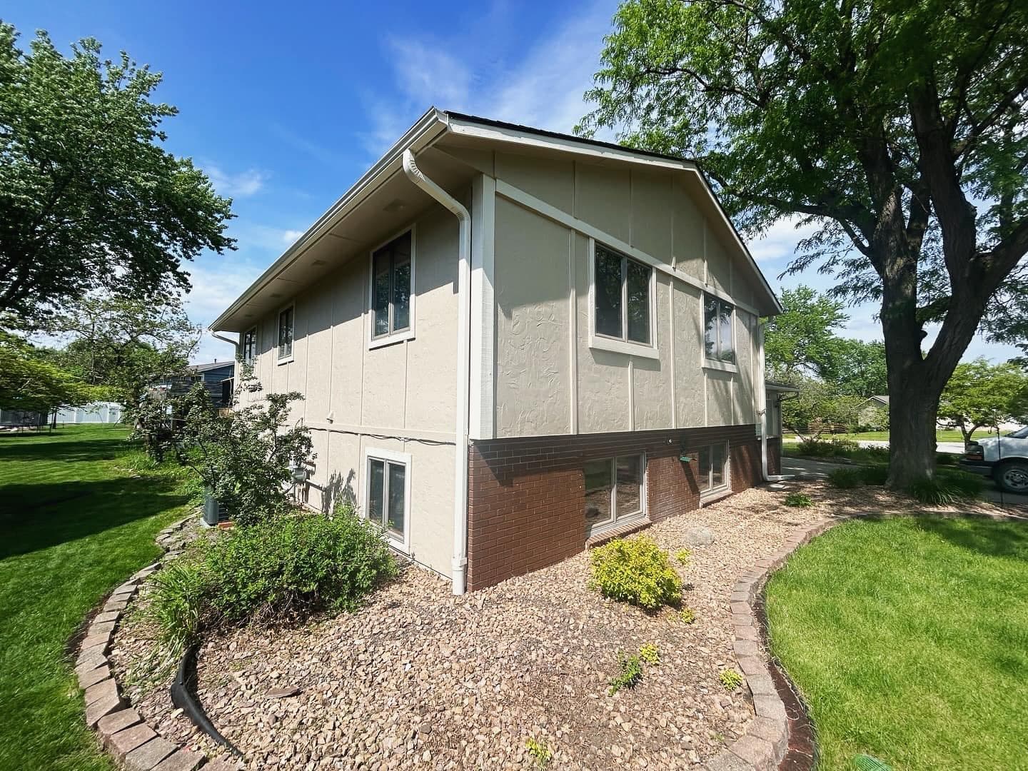 A repainted split-level home in warm tan and green with fresh white trim and edged landscaping beds.