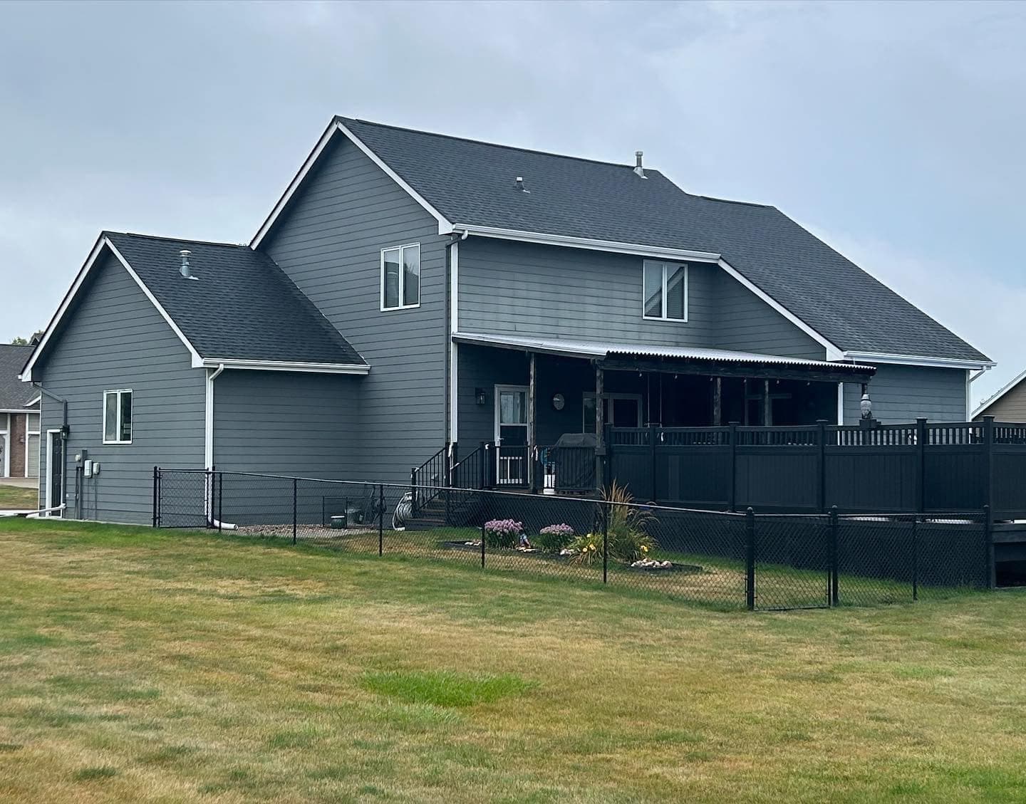 A gray-blue repainted exterior with white trim and a black aluminum fence enclosing the back yard.