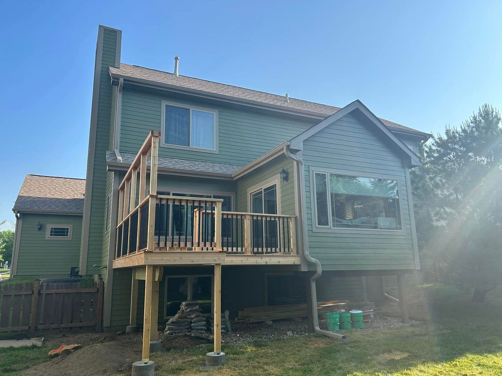 A repainted rear elevation in soft sage with white trim, wrapping around a raised deck and stair tower.