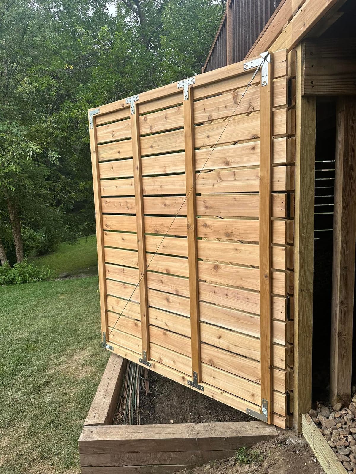 A horizontal cedar gate on strap hinges, hung within a matching privacy screen wall.