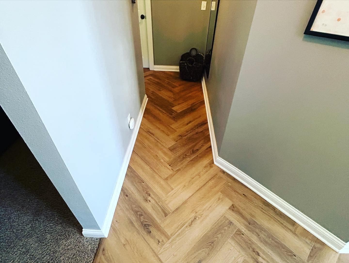 Luxury vinyl plank laid in a herringbone pattern, running from a doorway into an open room.