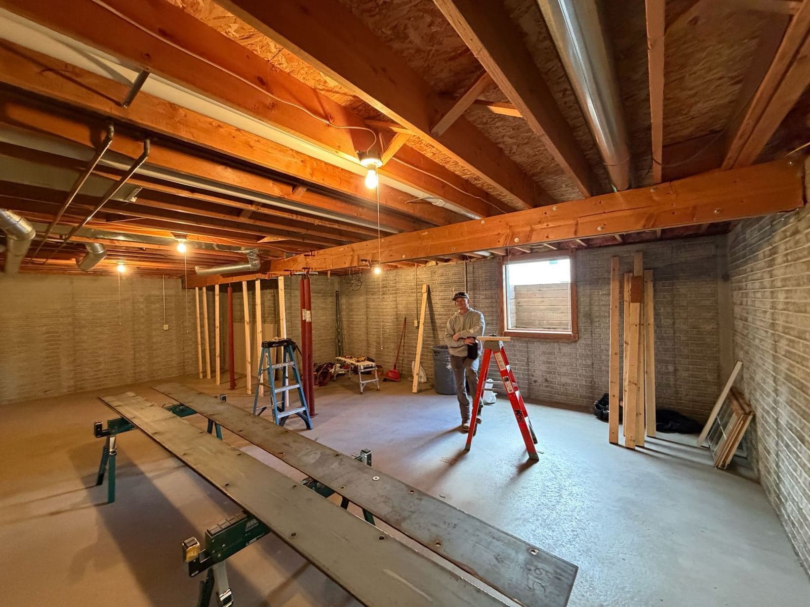 Basement framing in progress with new stud walls set beneath exposed floor joists and beams.