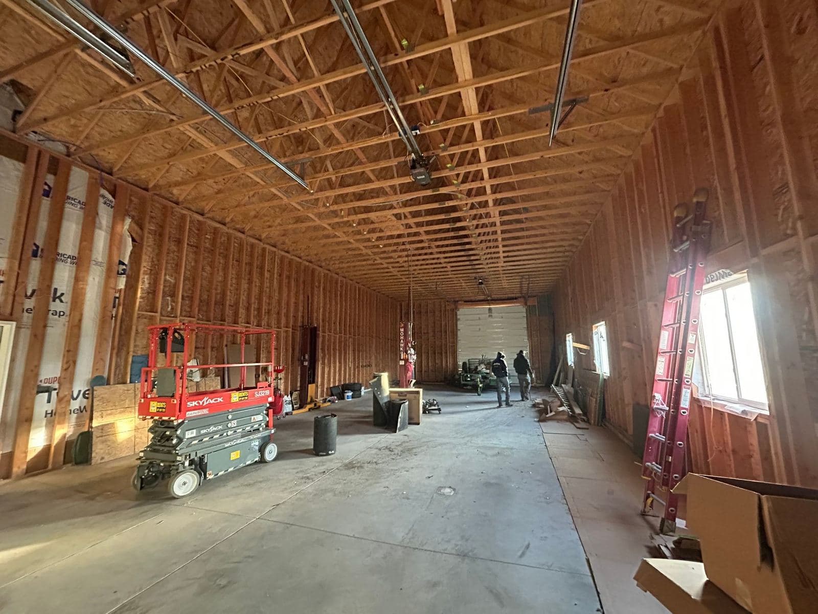 A garage framed and sheathed with open stud walls, roof trusses overhead and a scissor lift on the slab.