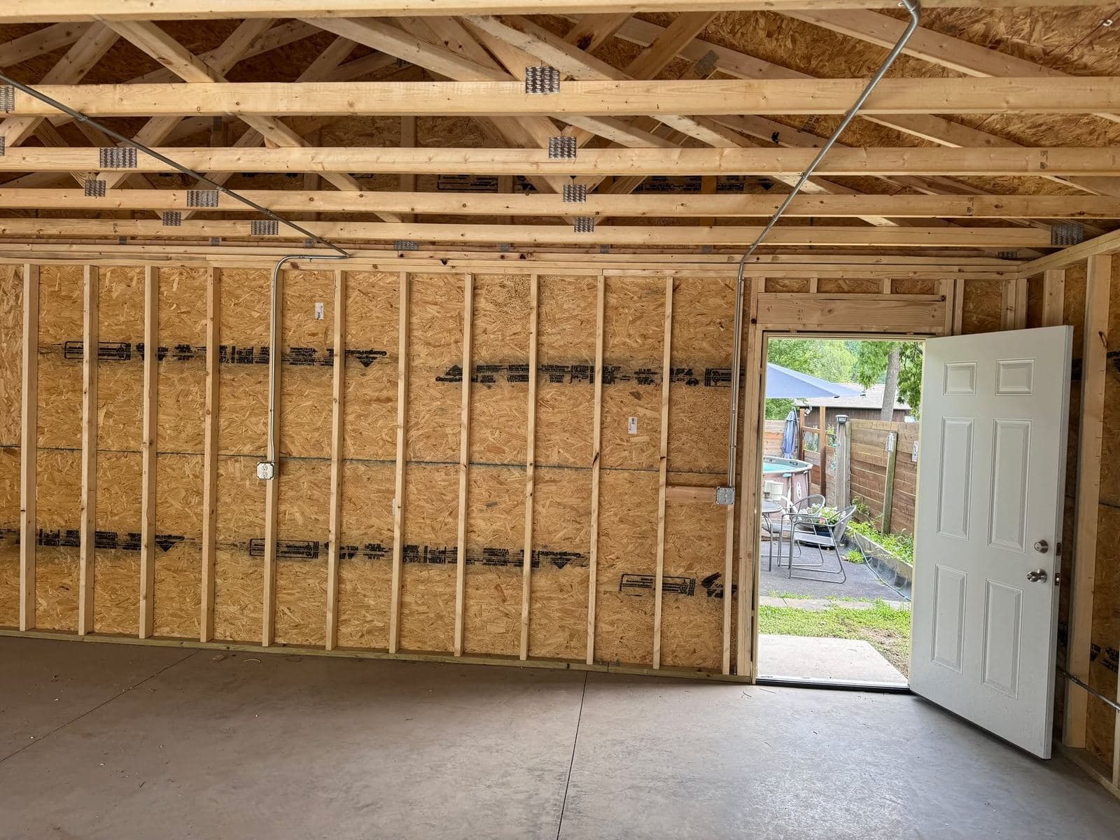 A framed garage wall with sheathing and a hung service door, seen from inside the finished slab.
