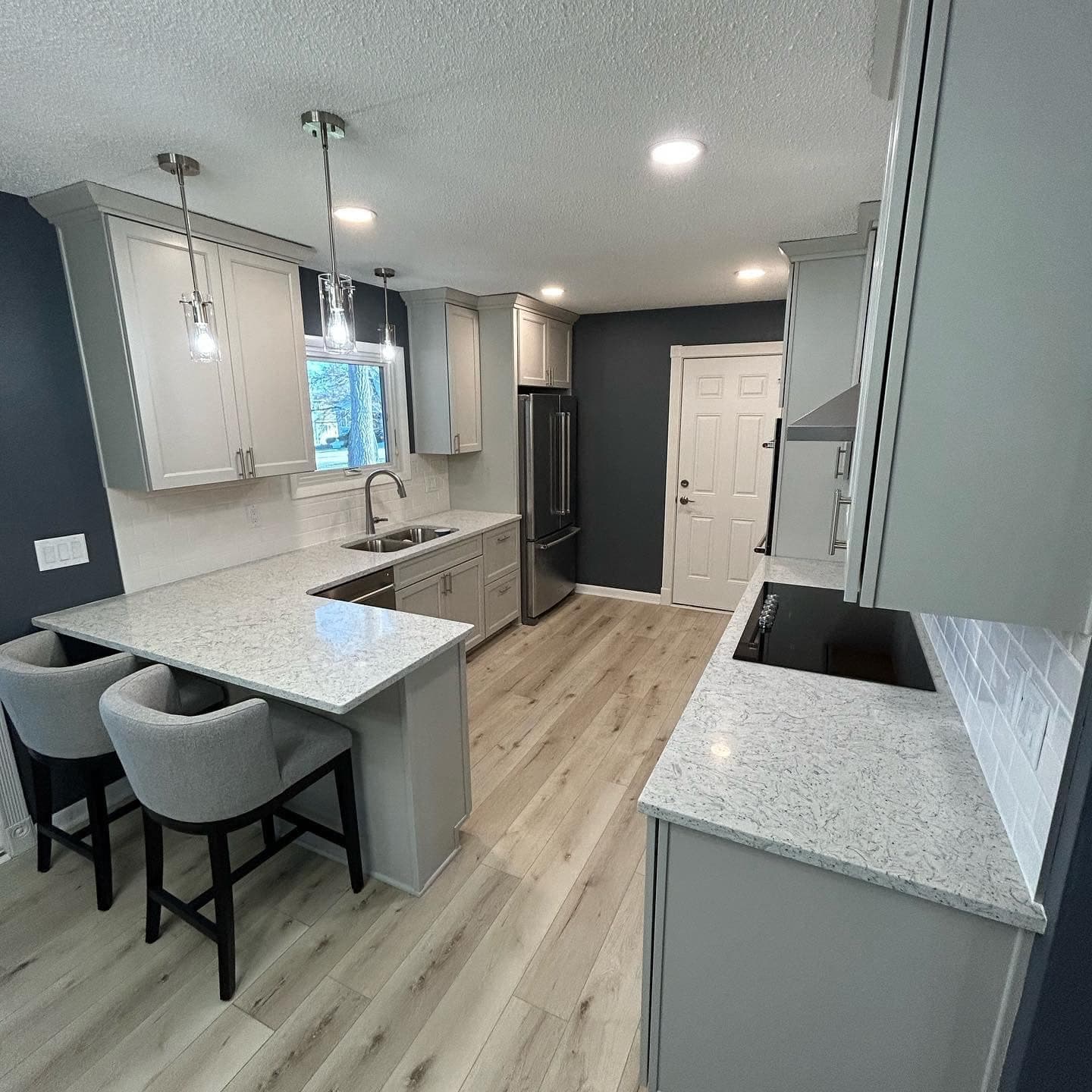 A gray and white kitchen with glass pendant lights over a quartz island and upholstered counter stools.