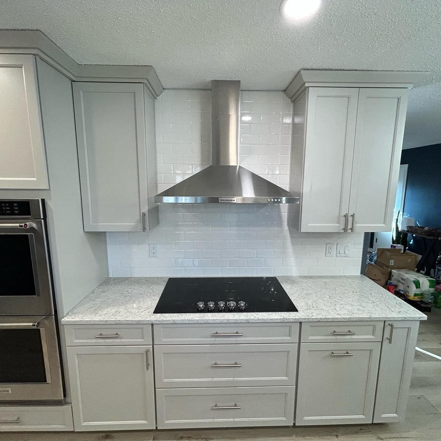 A white shaker kitchen with a stainless steel chimney hood, quartz counters and a built-in wall oven.