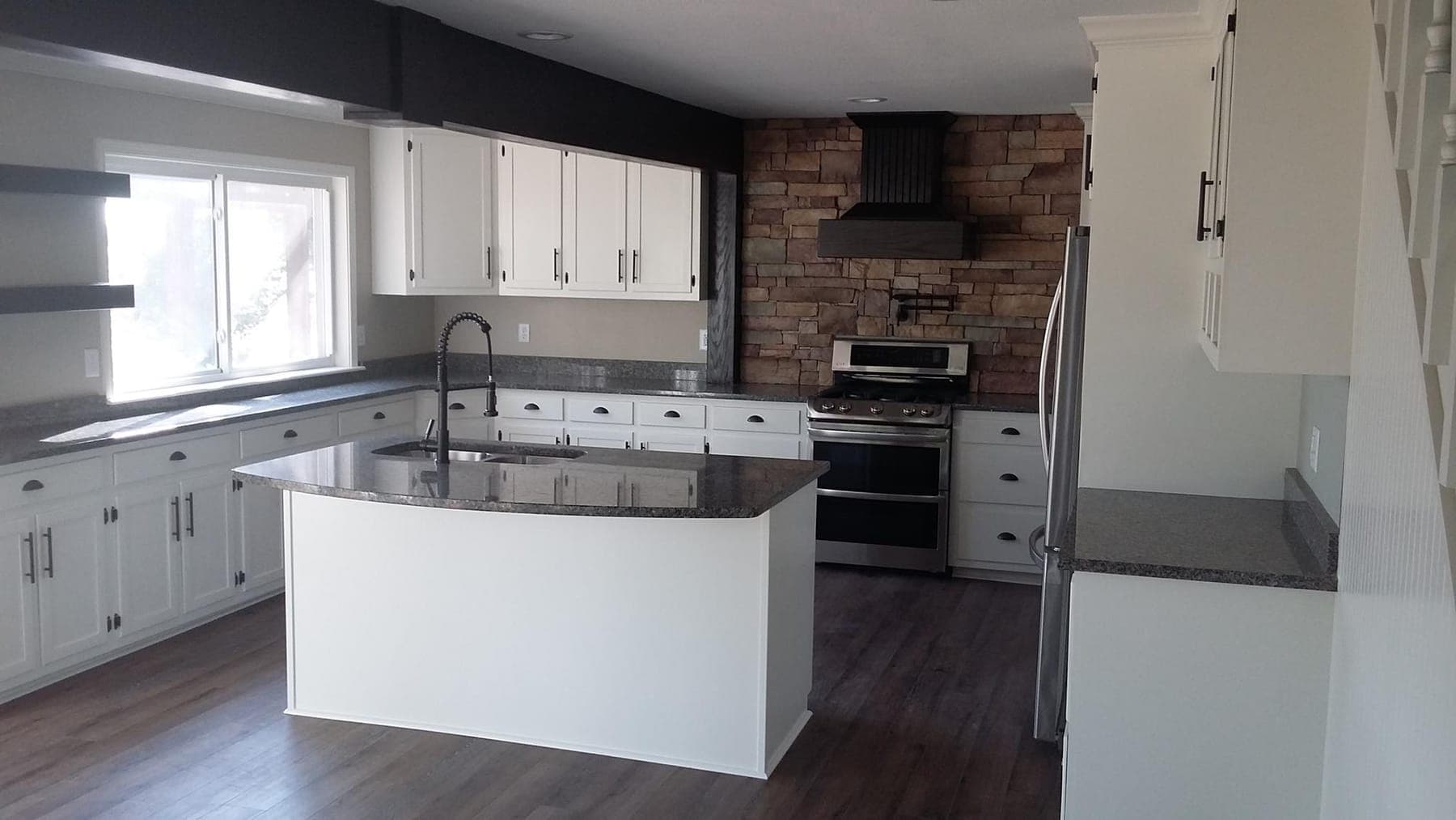 A white kitchen with a stone chimney breast and a granite island