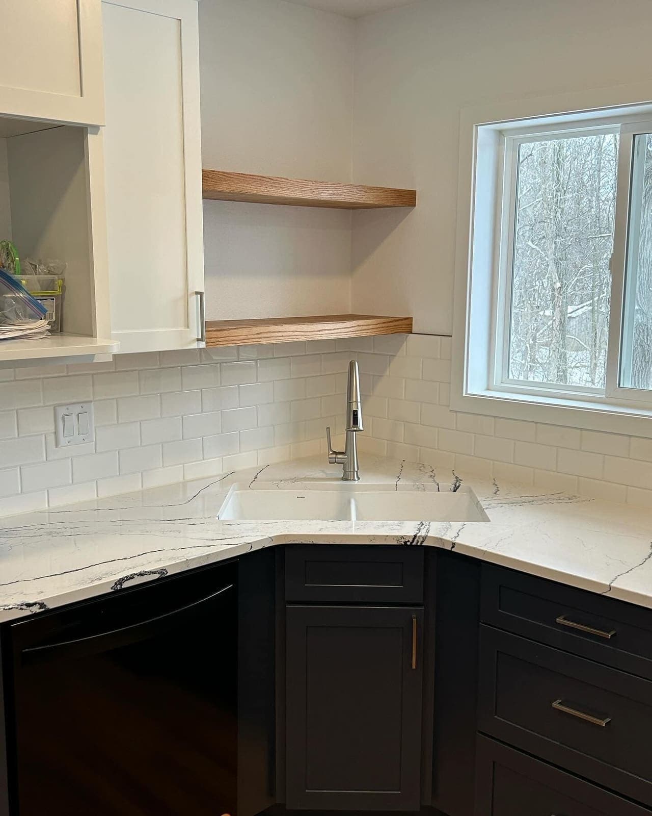 A kitchen corner with a marble-look counter, floating oak shelves and black lower cabinets.