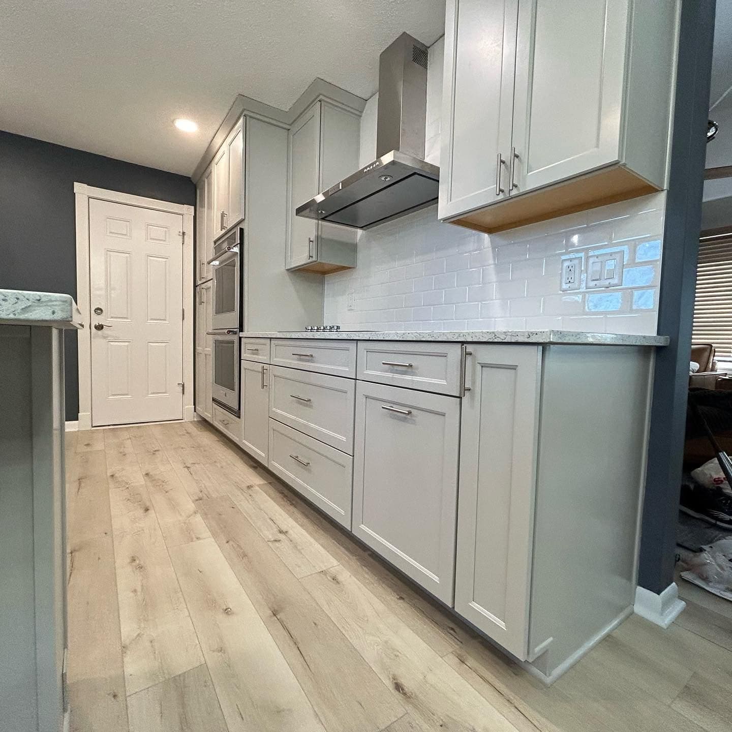 A run of grey cabinetry with a stainless chimney hood and a built-in double oven.
