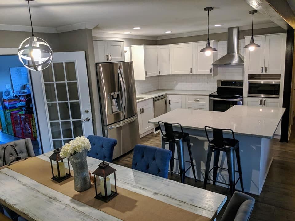 A finished kitchen in white shaker cabinetry with a quartz island, pendant lights and a stainless chimney hood.
