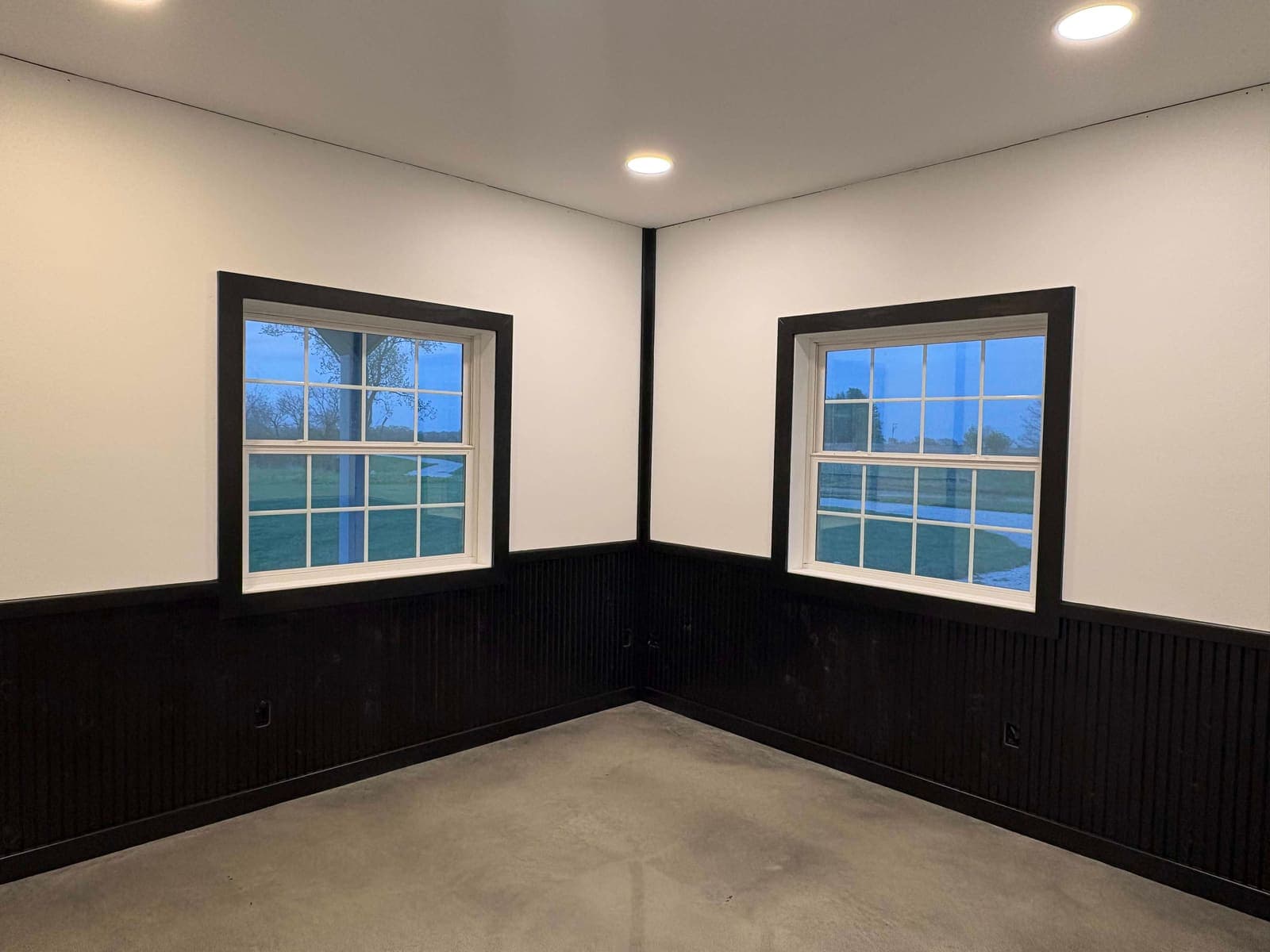 The corner of a two-tone room: white walls, black wainscot and two black-trimmed windows.