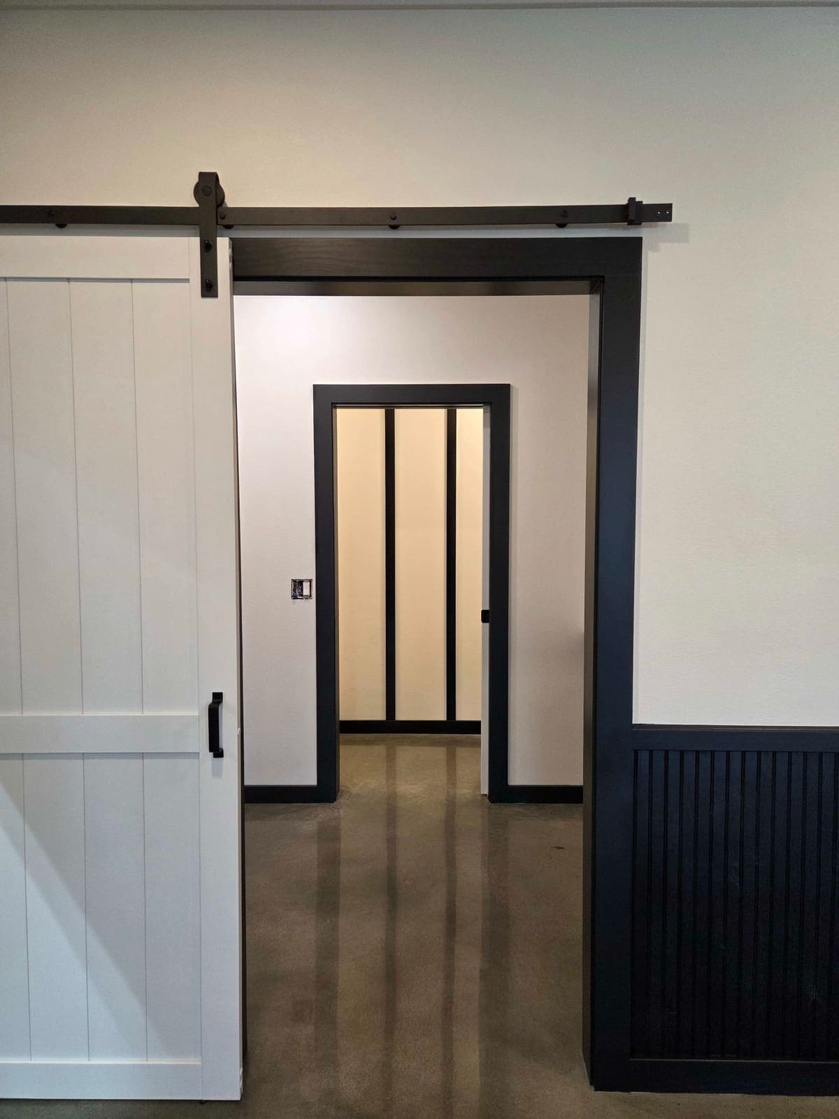 A white barn door beside a doorway painted black, opening to a glazed partition.